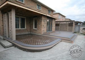 Image of a deck with curves and multiple levels. Trex Spiced rum decking and a custom stone privacy wall